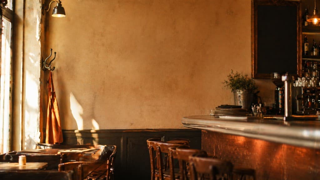 Salle de bistrot parisien en matinée, comptoir en zinc et chaises en bois, lumière chaude par la vitrine