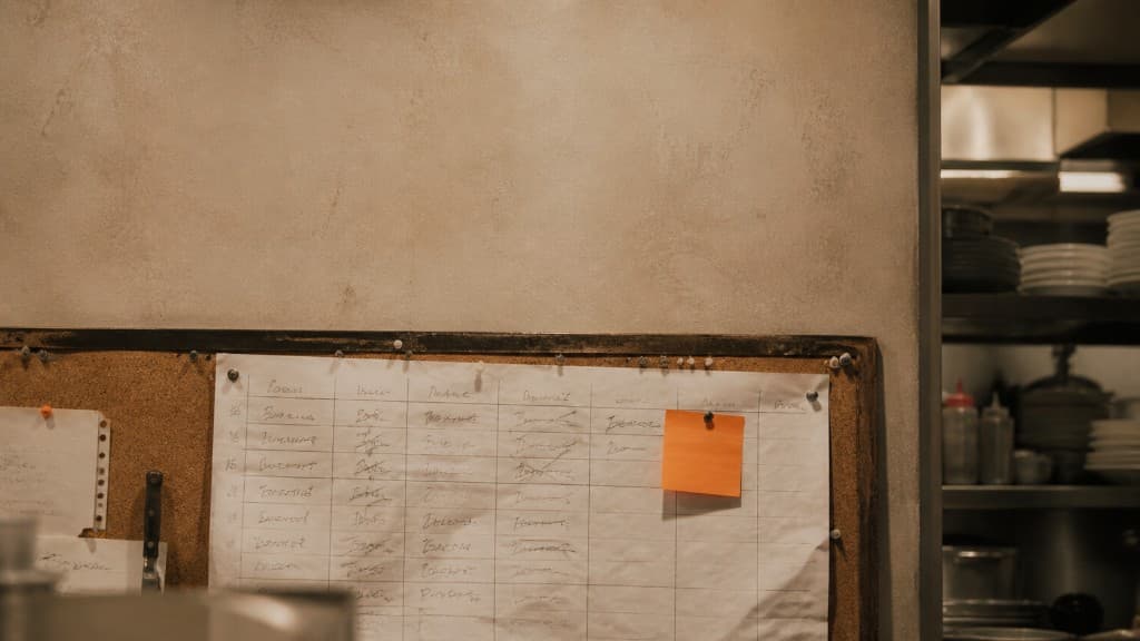 Tableau de planning hebdomadaire affiché en cuisine de restaurant avec un post-it orange